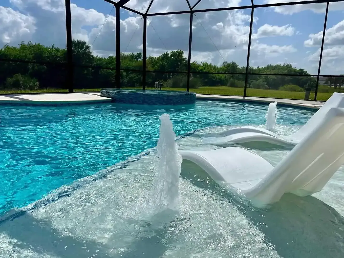 Poolside waterslide splashing into a bright blue pool under a screened enclosure and sunny sky