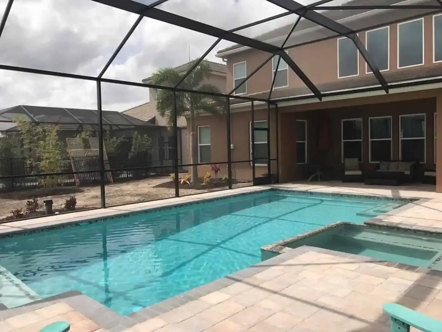 Backyard swimming pool with screened enclosure beside a brick house and patio seating