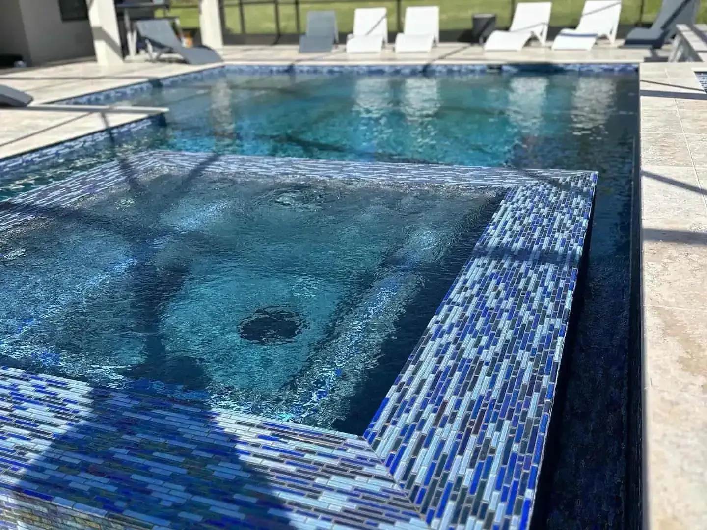 Blue mosaic swimming pool with a raised spa and lounge chairs in the background