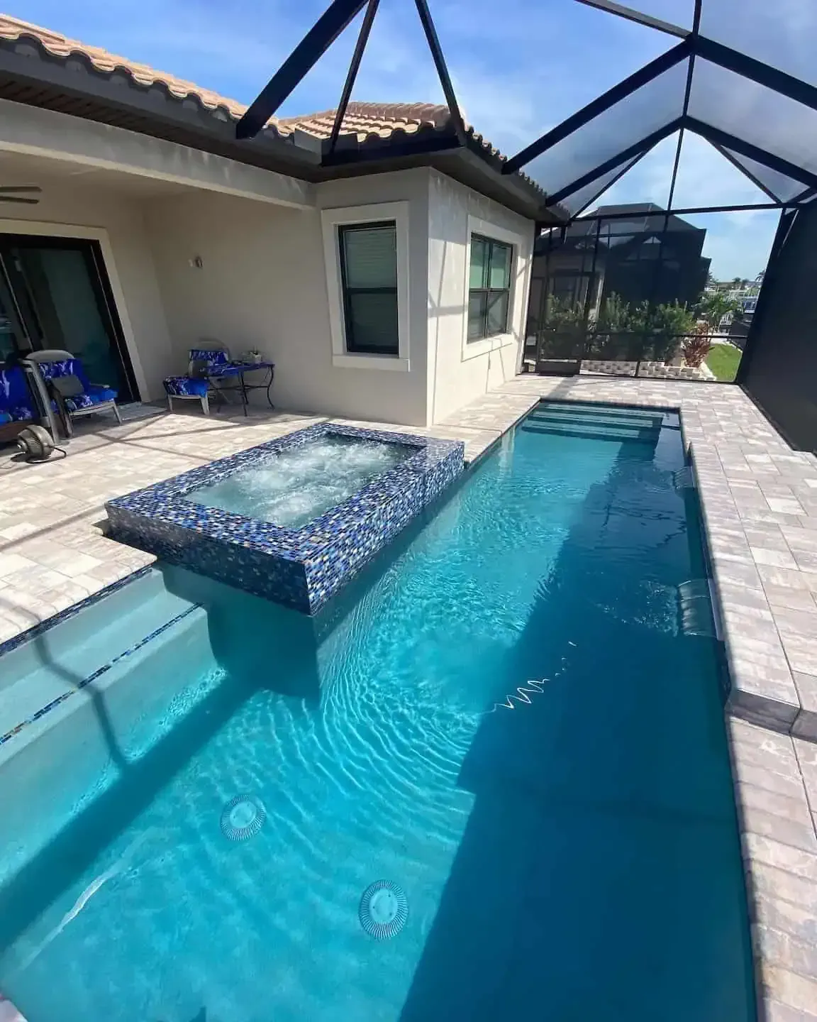 Backyard pool with a raised spa and screened patio beside a house under bright sunlight