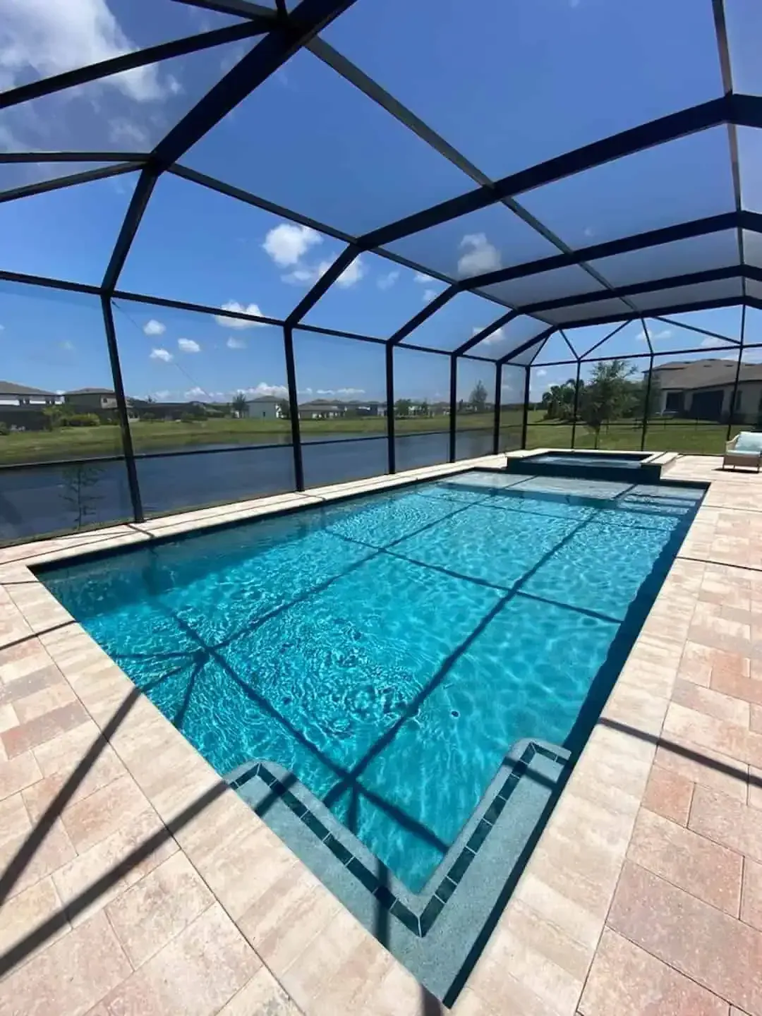 Covered backyard swimming pool with clear blue water and screened enclosure overlooking a grassy field