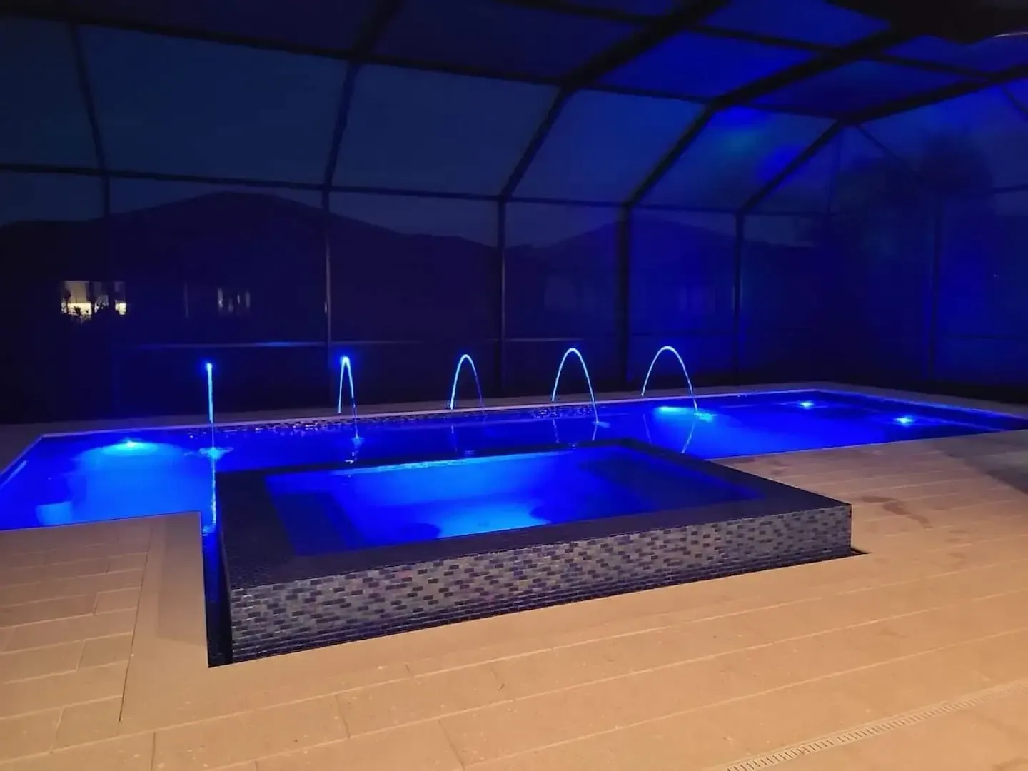 Blue-lit indoor pool with water jets and a raised spa at night