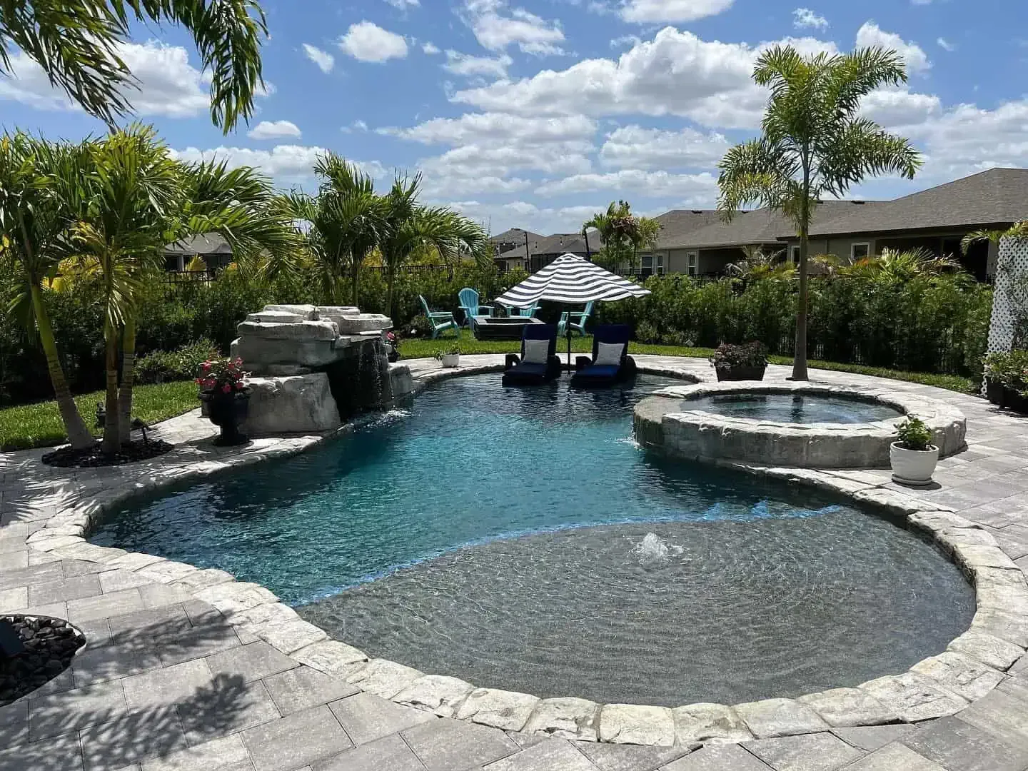 Backyard pool with stone spa, waterfall, and lounge chairs under a sunny sky