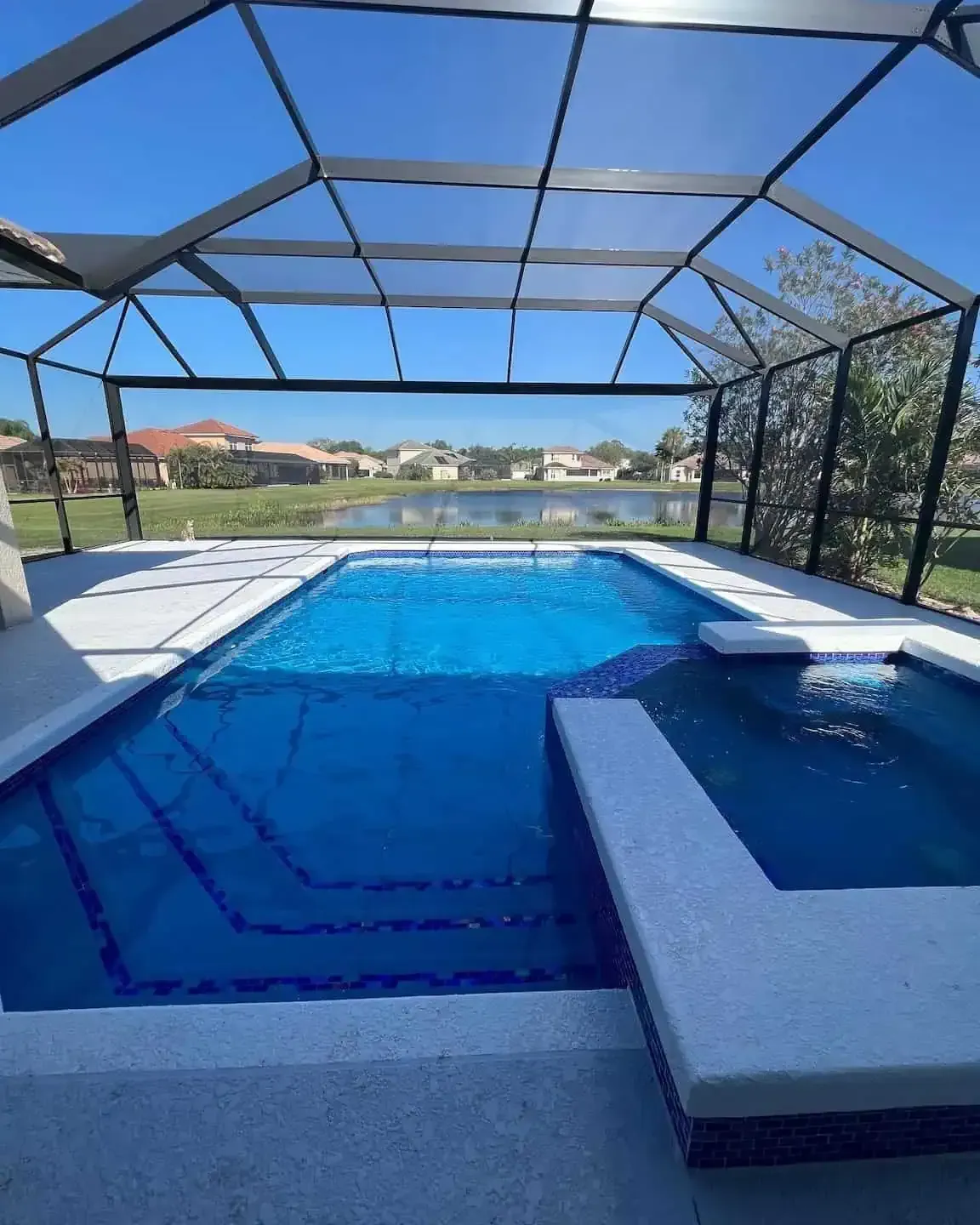 Screened backyard pool with blue water, hot tub, and covered patio overlooking a lake and houses