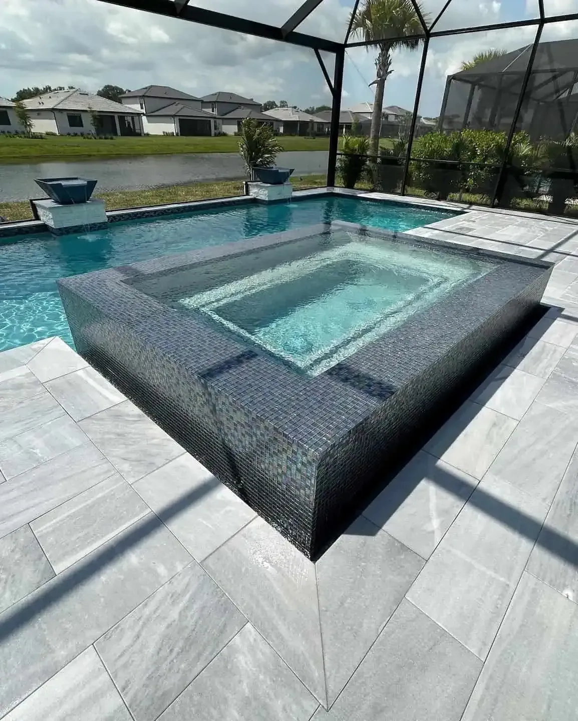 Modern backyard pool with a sunken hot tub, gray tile deck, and screened enclosure