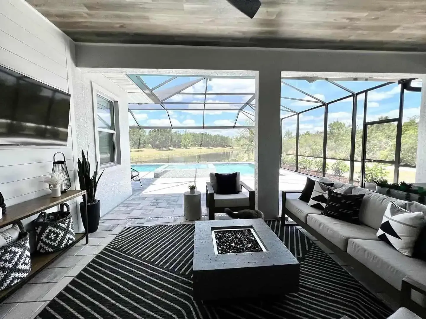 Modern screened patio lounge with sofa, fire pit table, and pool view
