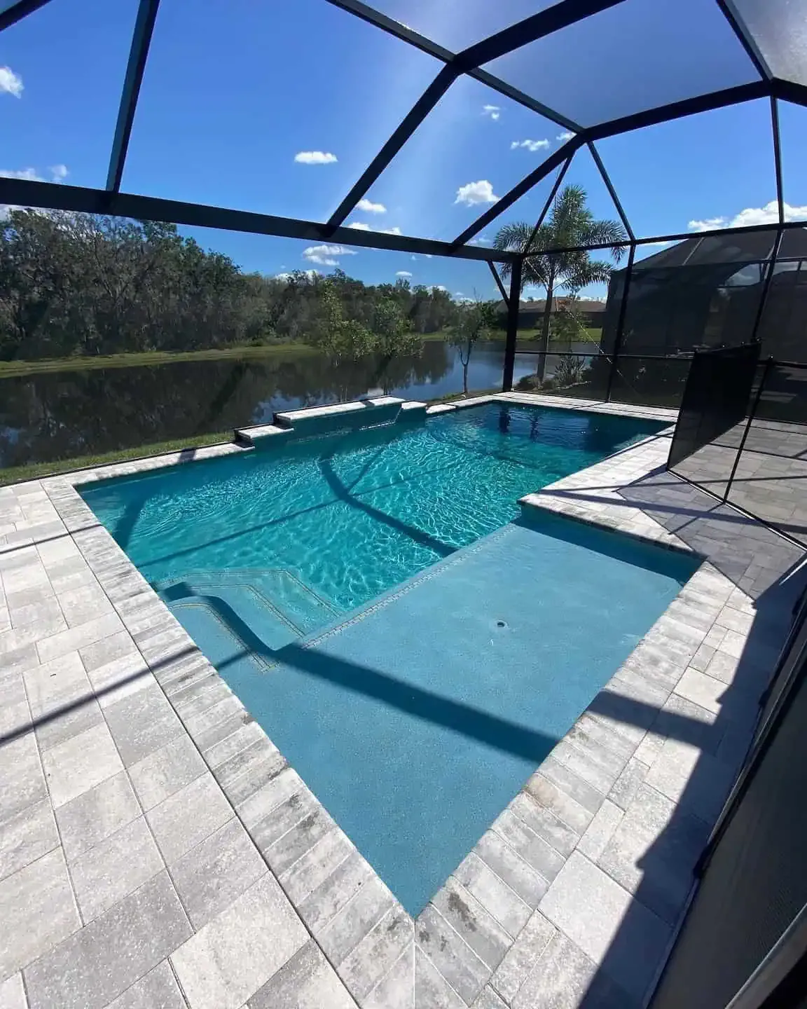 Screened-in backyard pool with turquoise water, stone deck, and sunny lake view