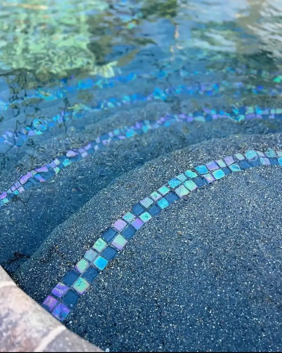 Blue mosaic steps descending into clear turquoise water in a pool or fountain