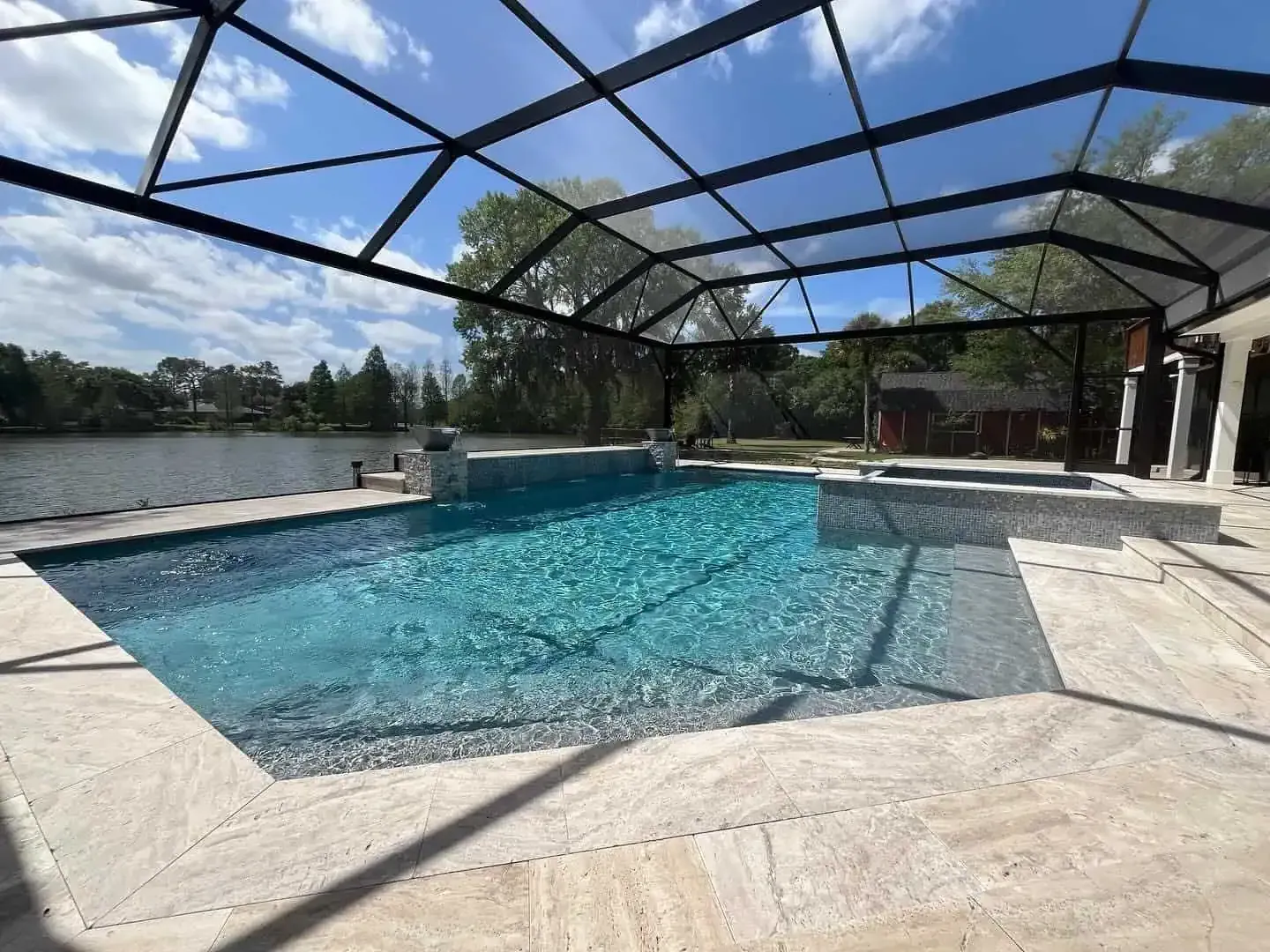 Outdoor swimming pool with blue water and a screened patio beside a lake under a bright sky