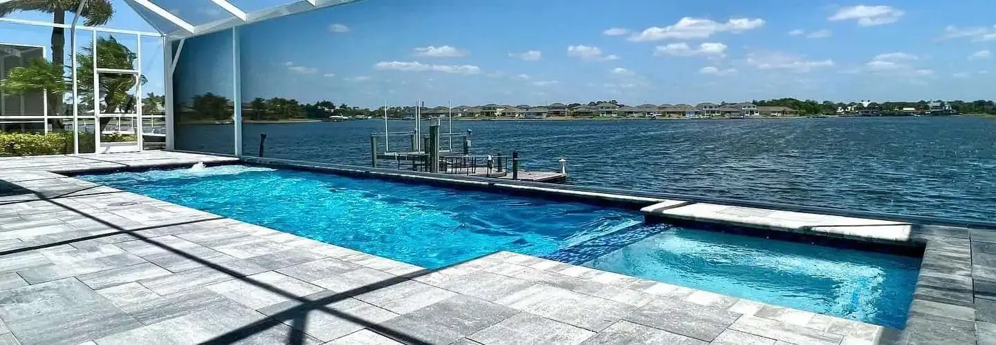 Modern infinity pool by the waterfront with glass railing and sunny blue sky