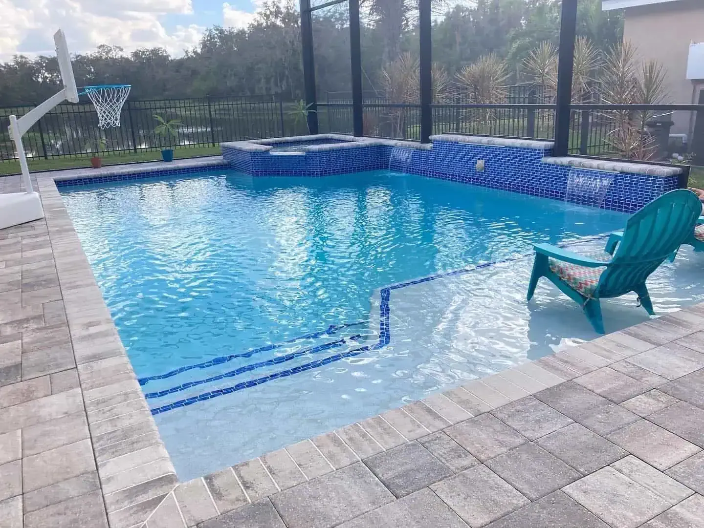 Backyard swimming pool with blue water, a teal chair, and a basketball hoop on the deck.