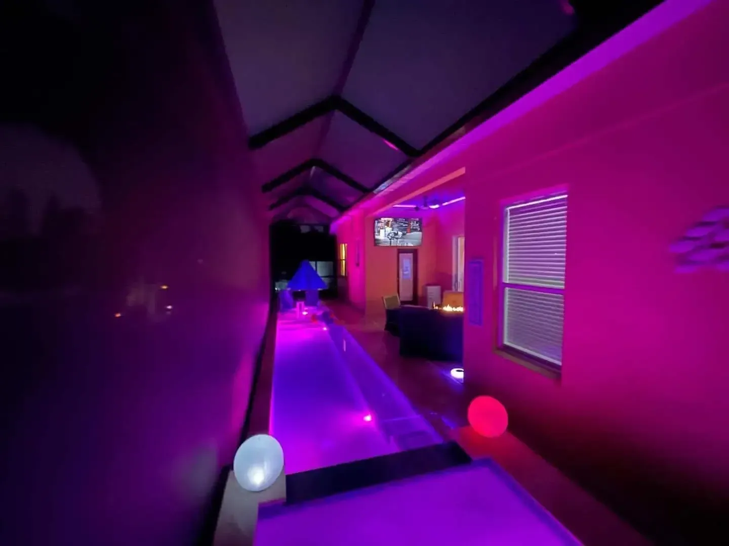 Purple-lit hallway with neon accents, wall blinds, and glowing orb lights at the entrance