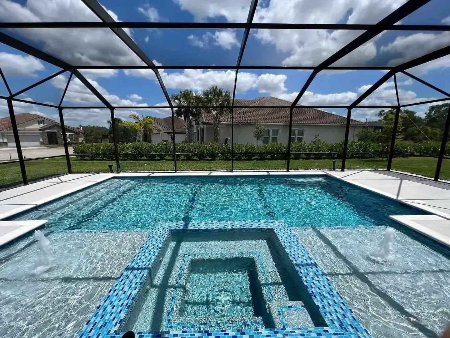 Backyard pool with blue water, screened enclosure, and submerged steps under a sunny sky