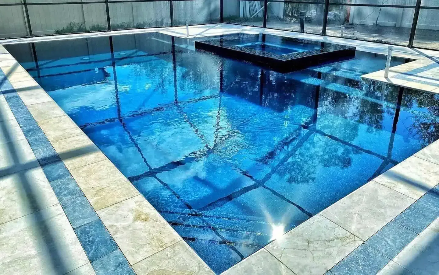 Blue indoor swimming pool with clear water, tiled deck, and a raised platform in the center