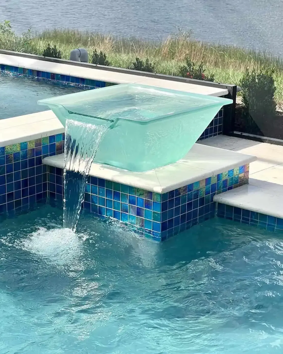 Blue-tiled pool fountain spilling water from a glass-like basin into a swimming pool