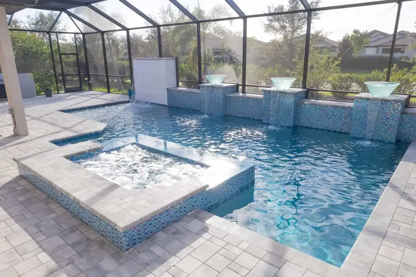 Outdoor pool with a raised spa, blue water, and screened enclosure on a tiled patio