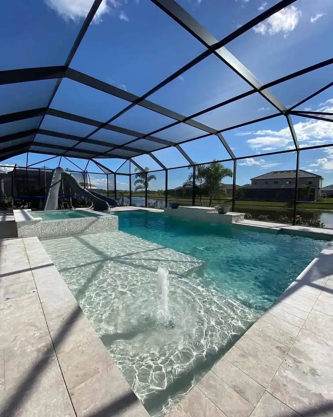 Backyard pool under a screened enclosure with bright blue water and a sliding pool ramp