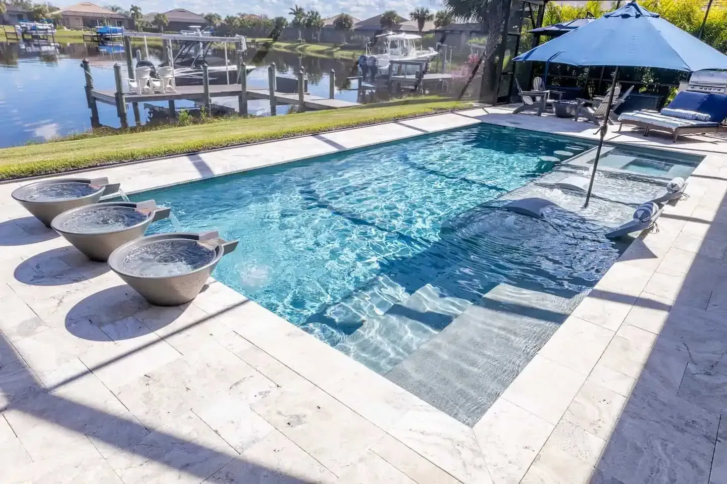Poolside patio with a blue umbrella, built-in spa, and waterfront view.