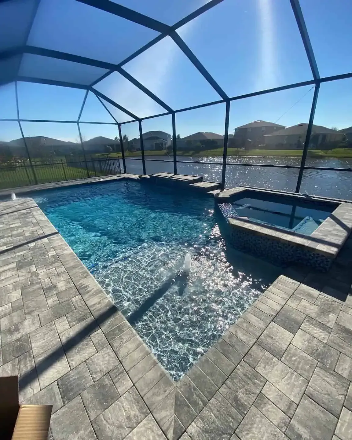 Screened-in backyard pool and spa with blue water, stone deck, and mountain view under clear sky