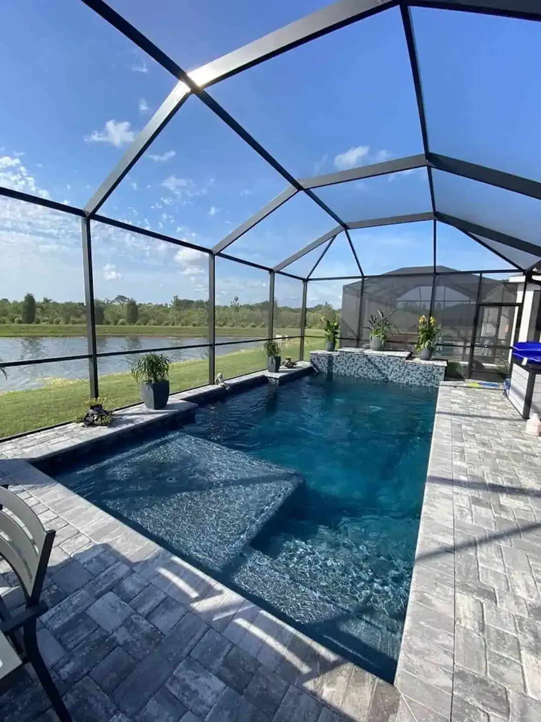 Screened-in backyard pool with paver deck and lake view under a sunny sky