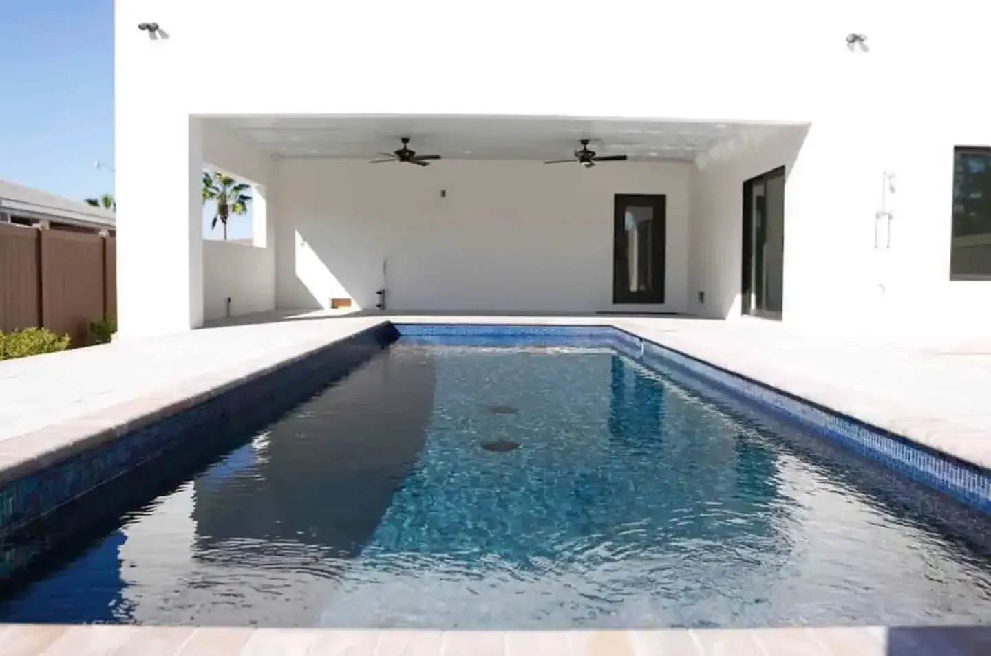 Modern backyard with a rectangular swimming pool beside a covered patio and white house exterior