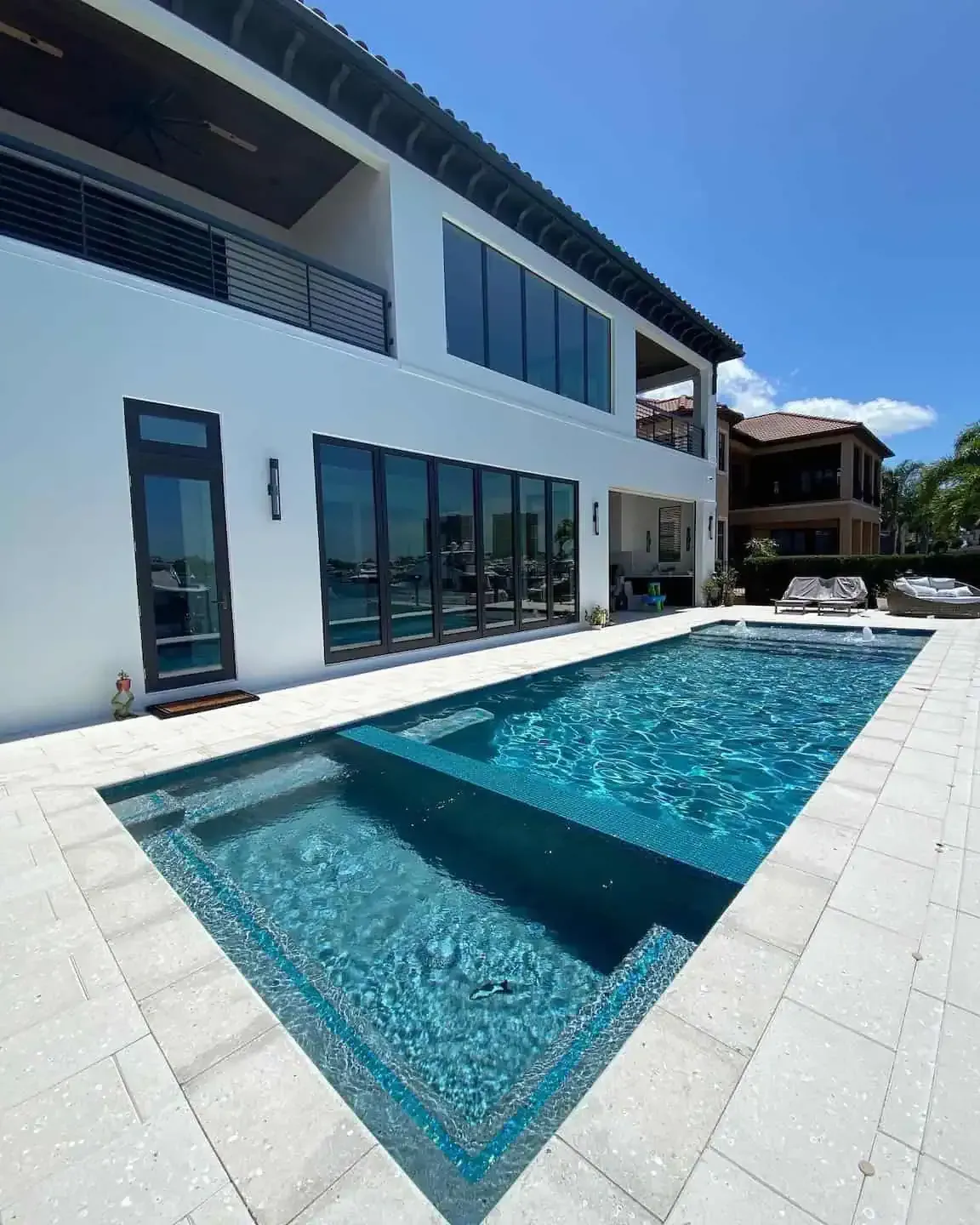 Modern white villa with large windows beside a blue swimming pool under a clear sky