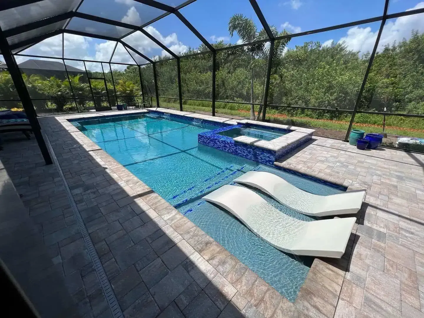 Screened backyard pool with blue water, stone deck, and two white lounge chairs