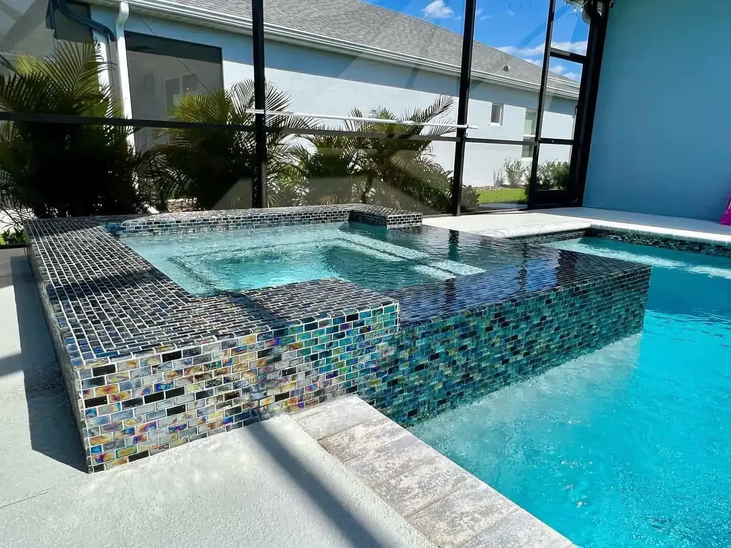 Mosaic-tiled hot tub beside a bright blue resort pool, with palm trees and lounge seating nearby