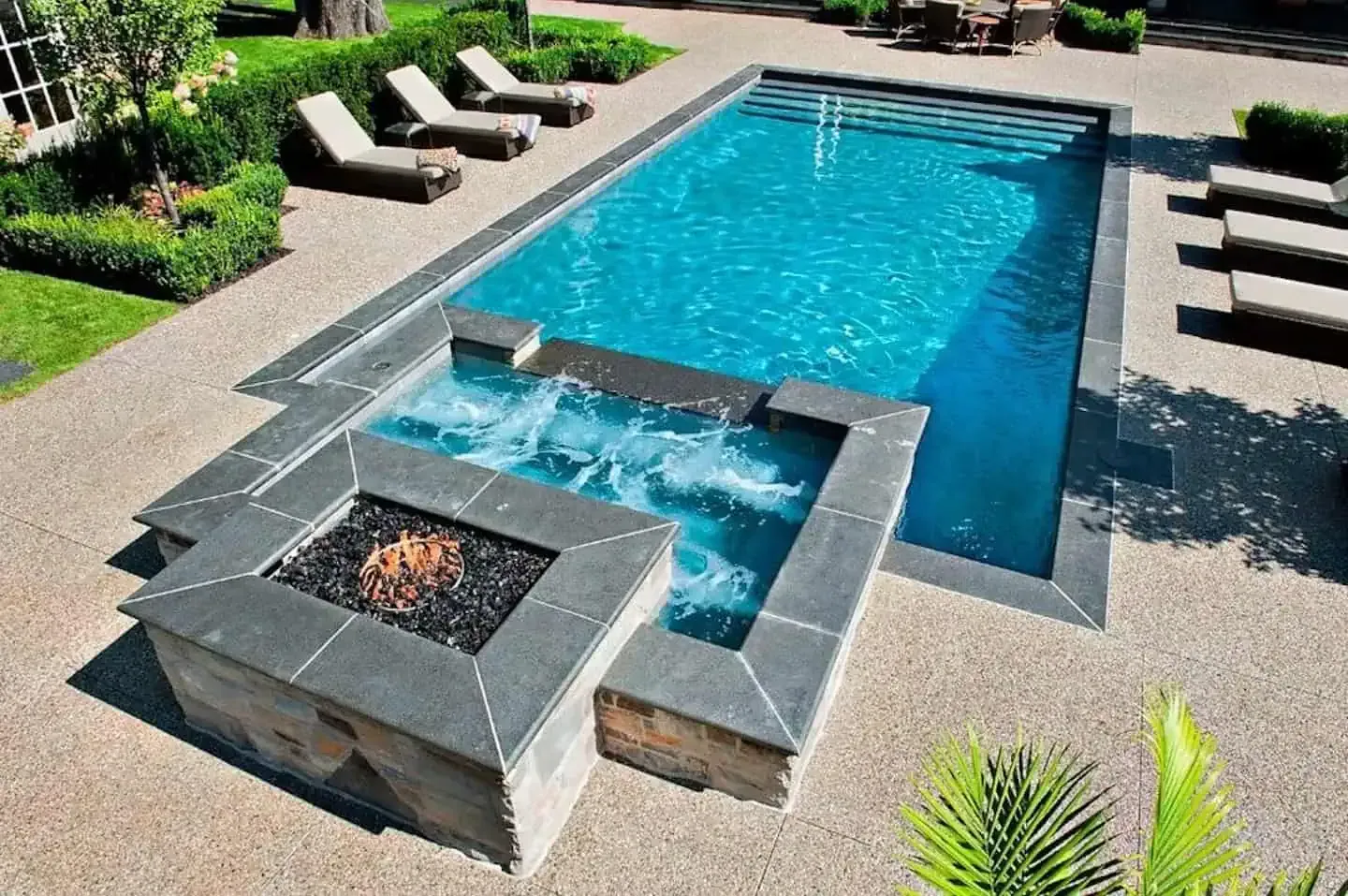 Modern backyard pool with a built-in fire feature and lounge chairs surrounding it