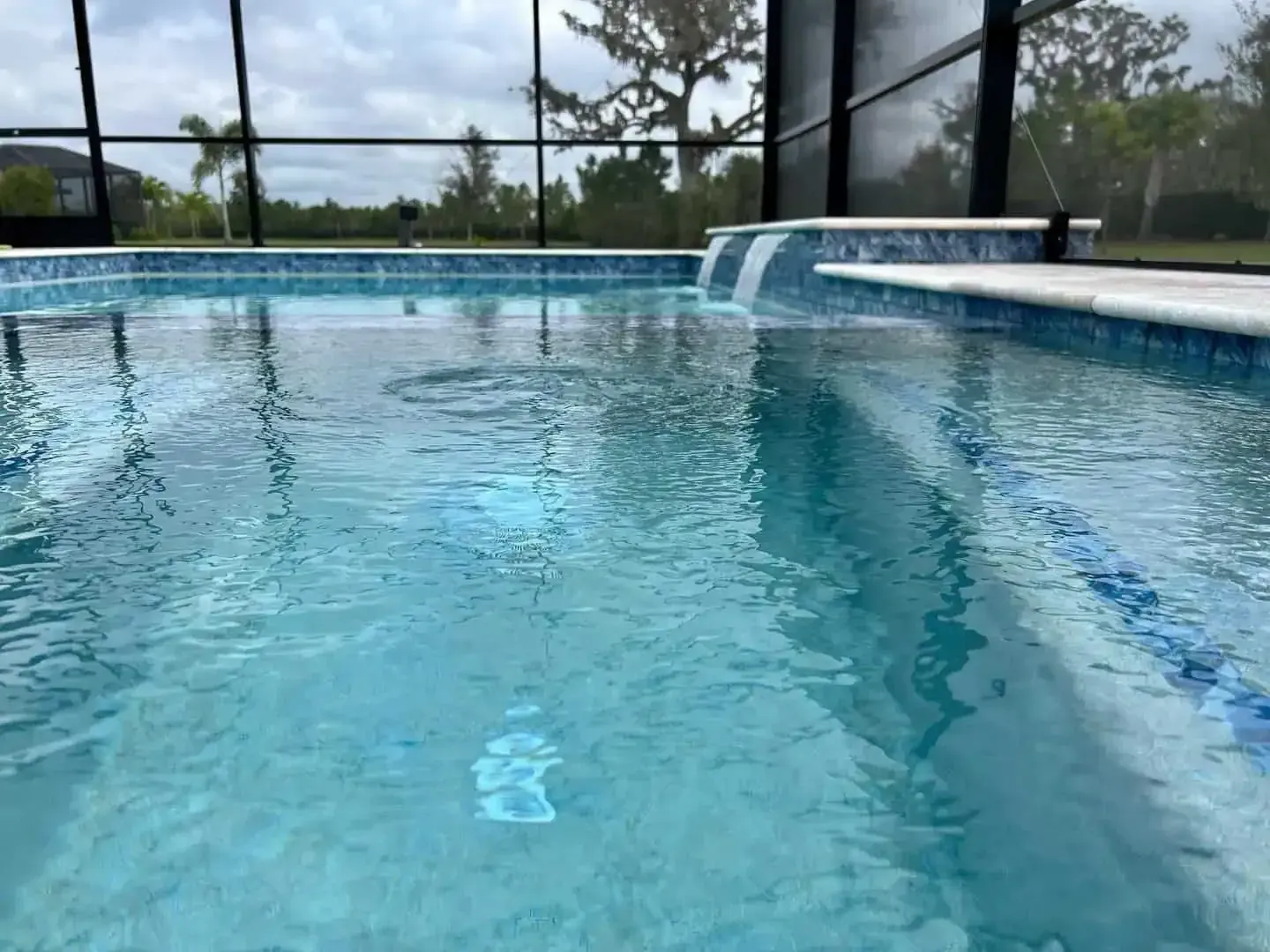 Clear blue swimming pool with water feature and screened enclosure outdoors