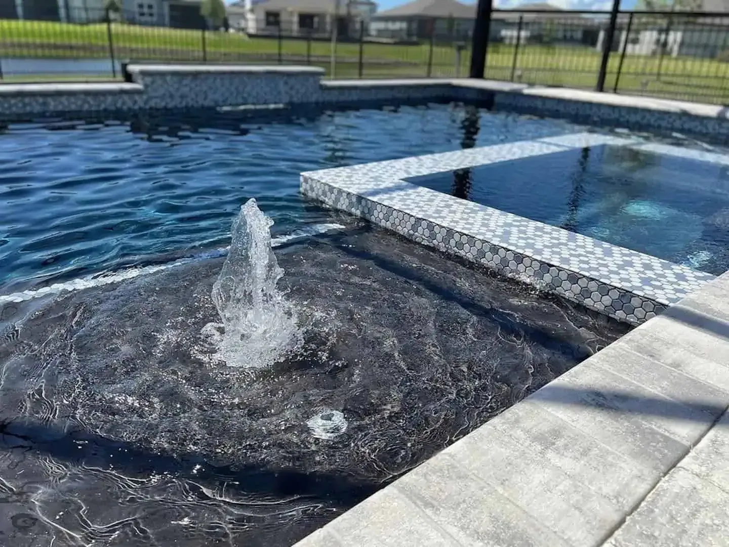 Pool with bubbling fountain and raised tiled spa beside blue water, beside a fenced patio