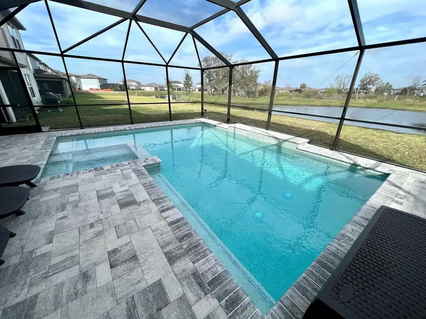 Screened-in backyard pool with turquoise water and a gray patio overlooking a grassy yard and canal