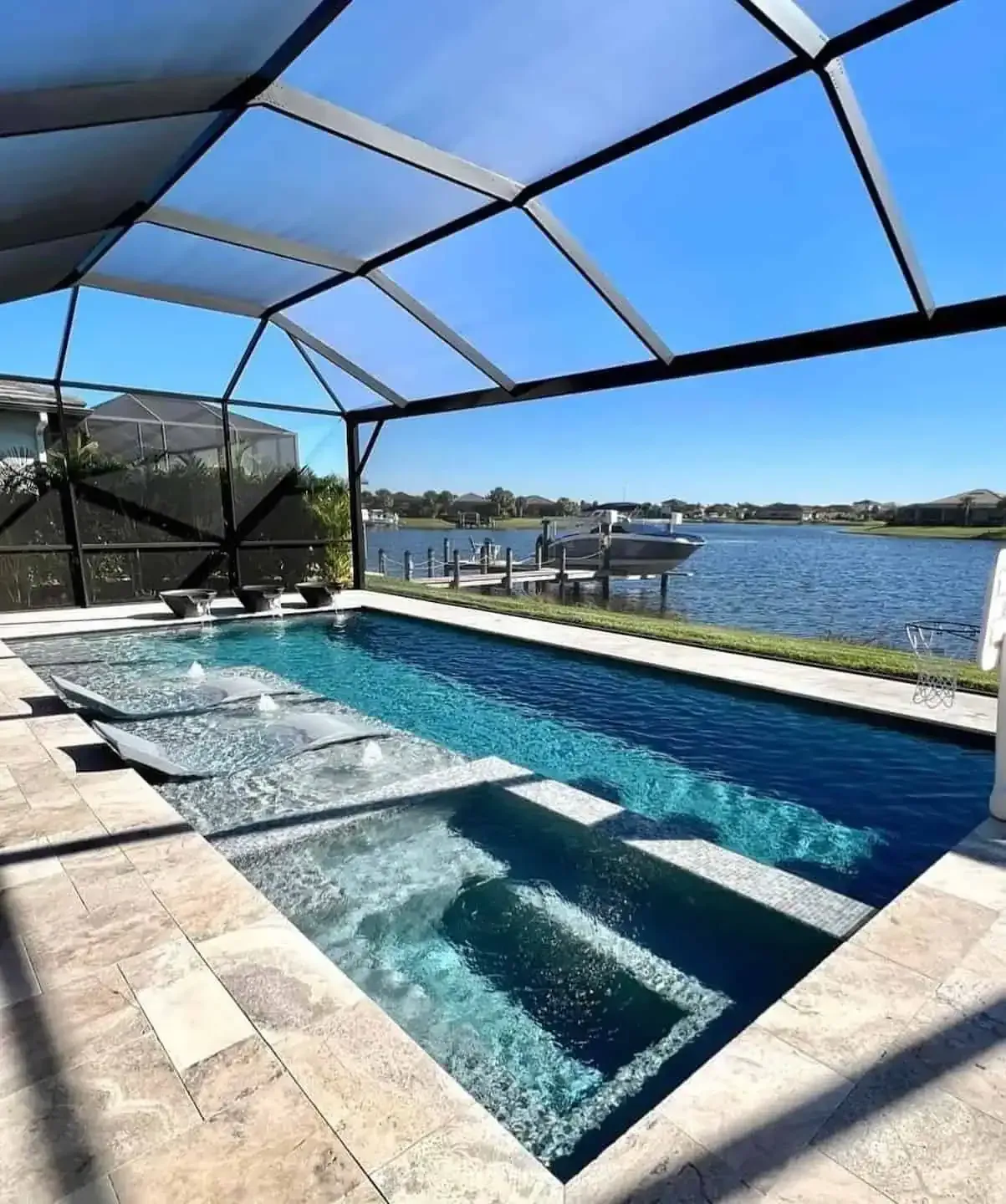 Covered pool overlooking a lake, with blue water, stone deck, and screened enclosure