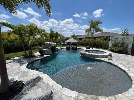 Luxury backyard pool with spa, stone deck, and tropical landscaping under a sunny blue sky