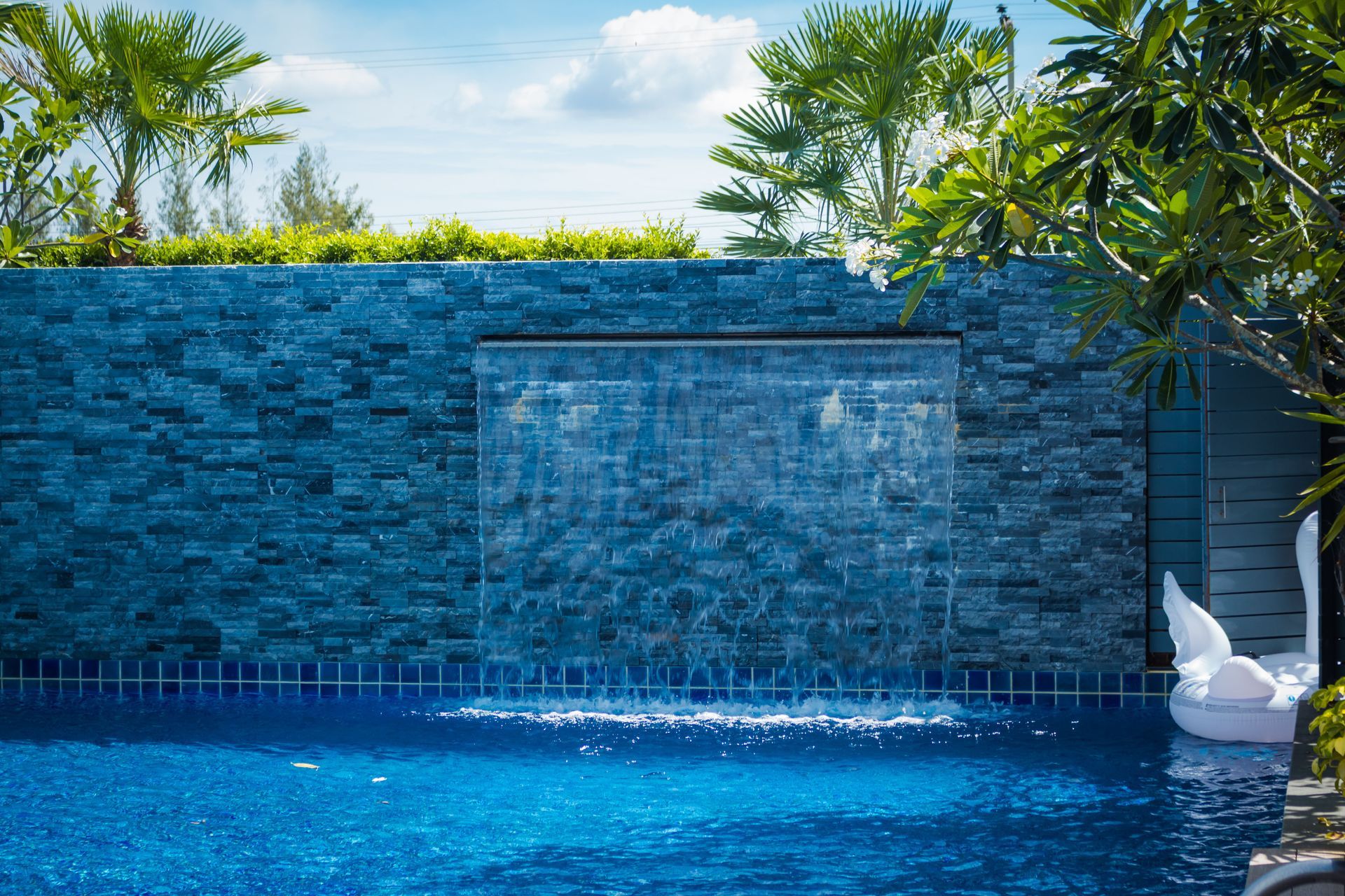 Blue tiled pool waterfall with a white swan float and tropical greenery