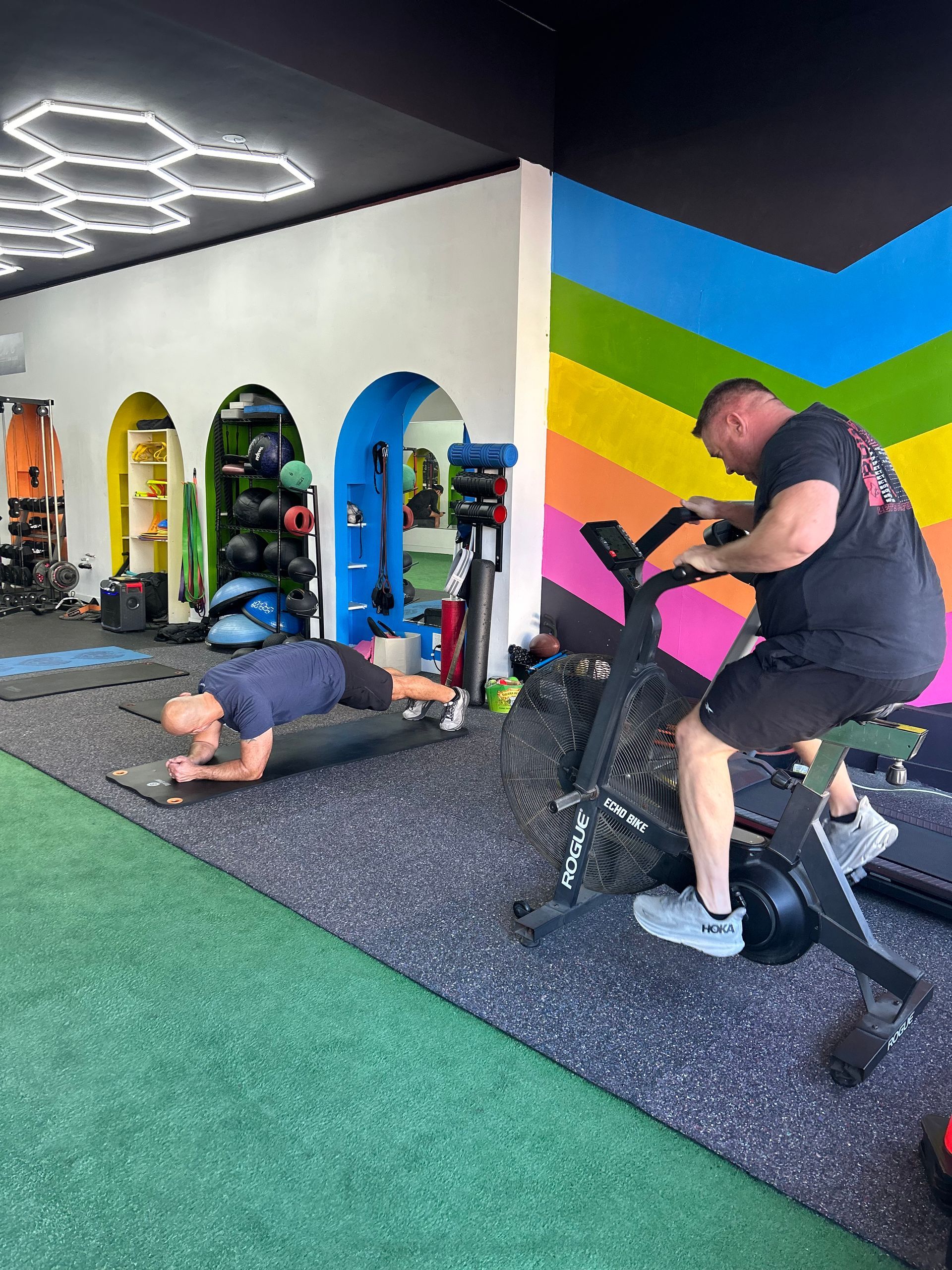 A man is doing push ups while another man is riding an exercise bike in a gym.