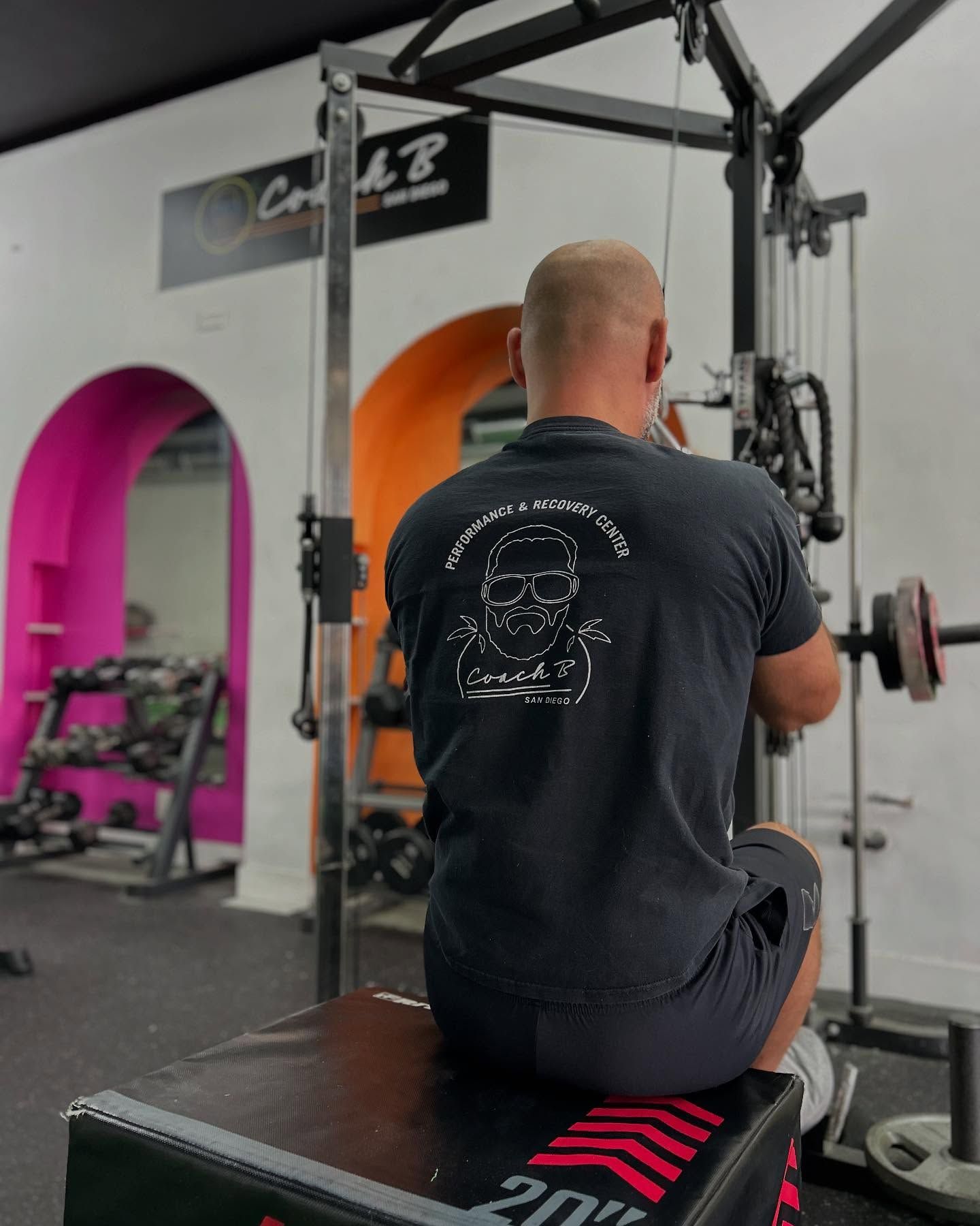 A man in a black shirt is sitting on a box in a gym