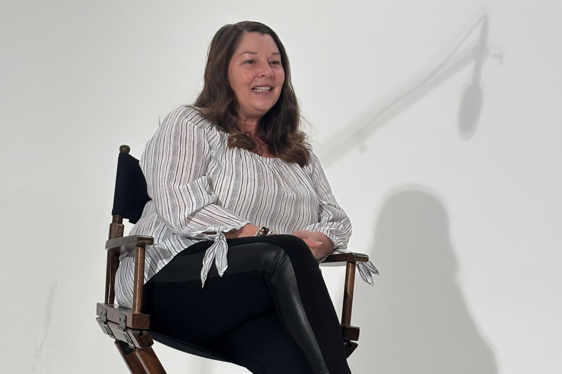 Woman seated in a director’s chair, smiling against a plain white background.