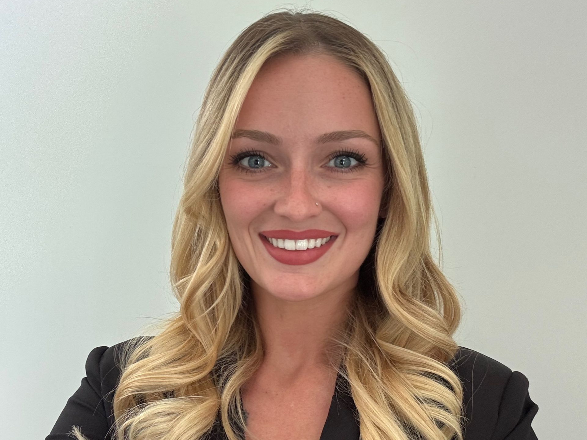 Smiling blonde woman in a black blazer against a light background