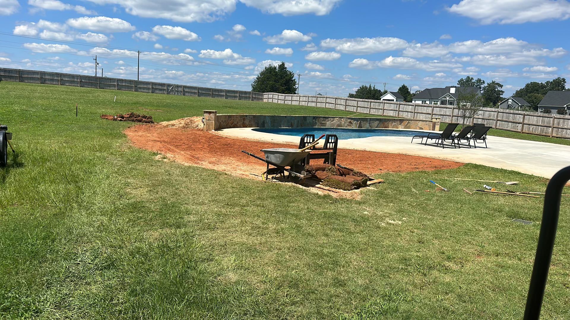 A wheelbarrow is sitting in the grass in front of a swimming pool.