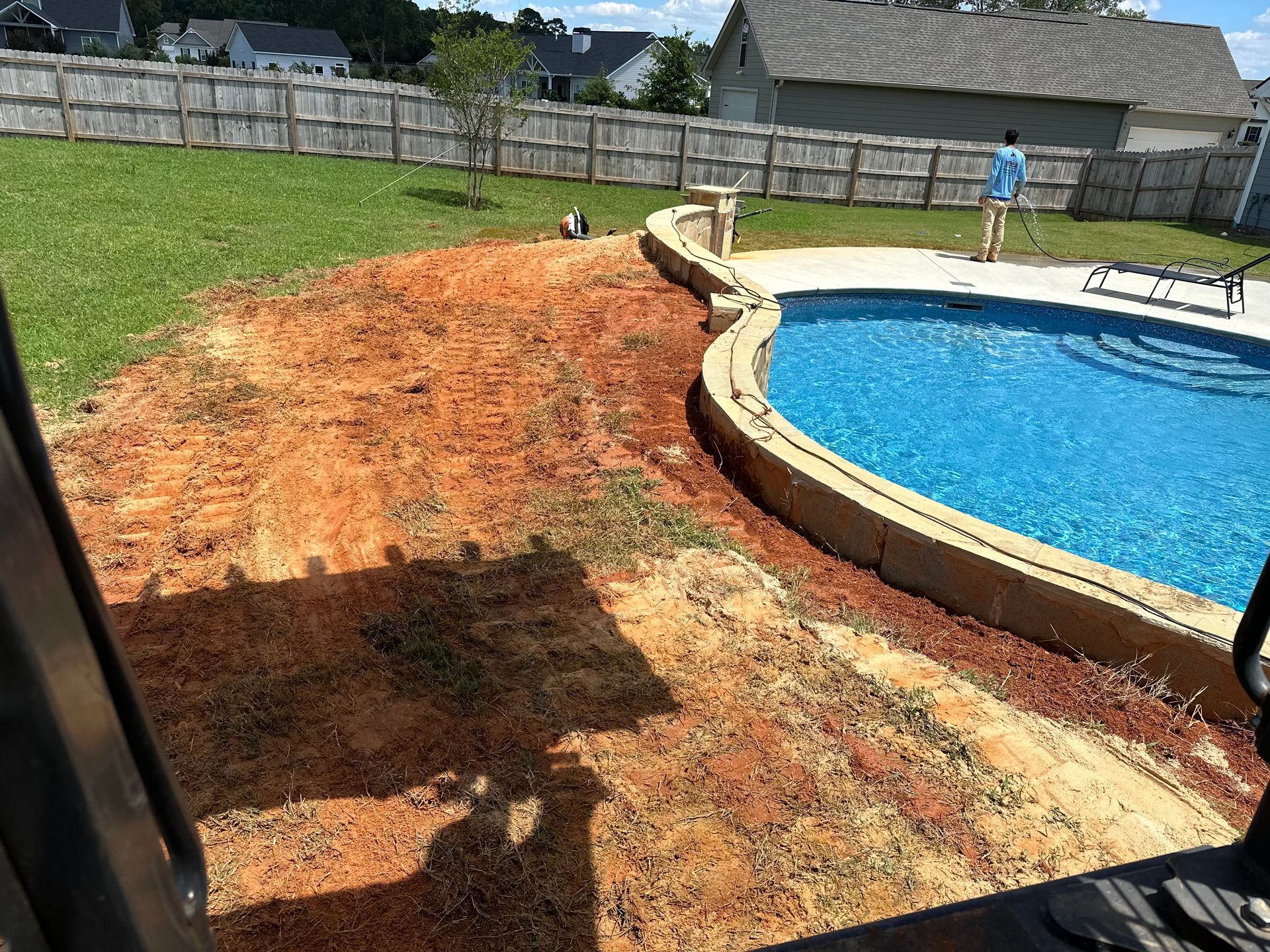 A man is standing next to a swimming pool in a backyard.