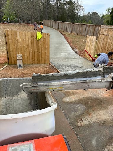 A man is working on a concrete walkway next to a wooden fence.