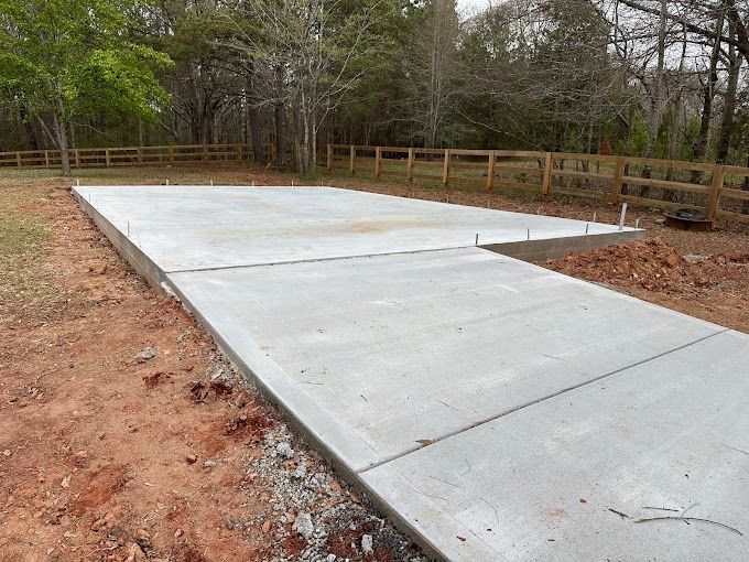 A large concrete slab is sitting in the middle of a dirt field next to a wooden fence.