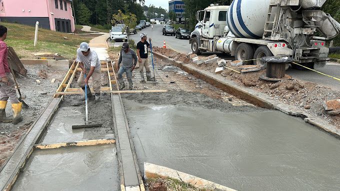 A group of construction workers are working on a sidewalk next to a concrete mixer truck.