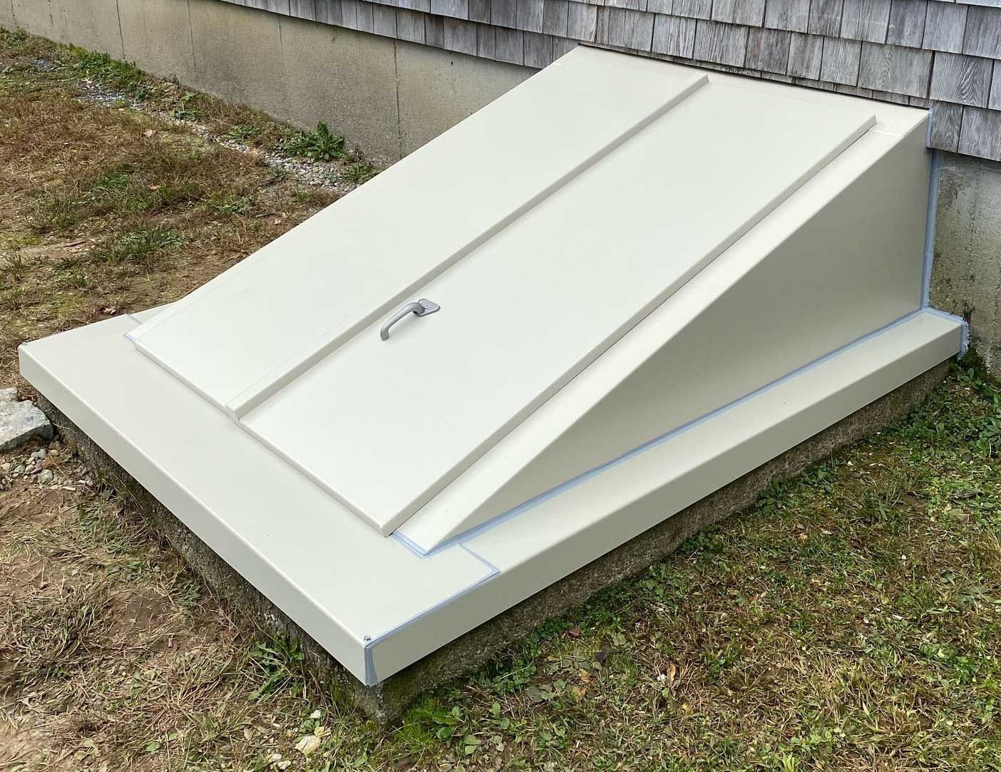 Beige, slanted basement door on a concrete foundation, next to a building with gray siding.
