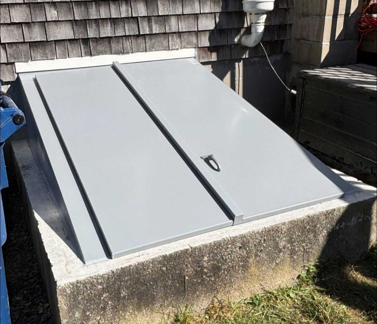 Gray metal cellar doors set in concrete foundation against a wood-paneled wall.