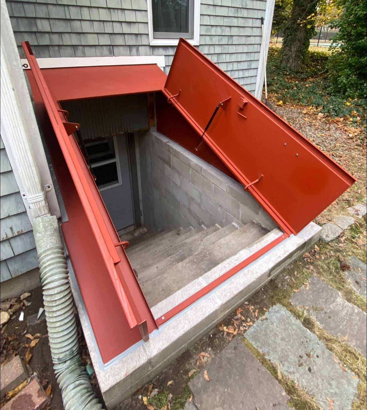 Red metal doors open to basement stairs. Gray concrete steps descend into a dark doorway.