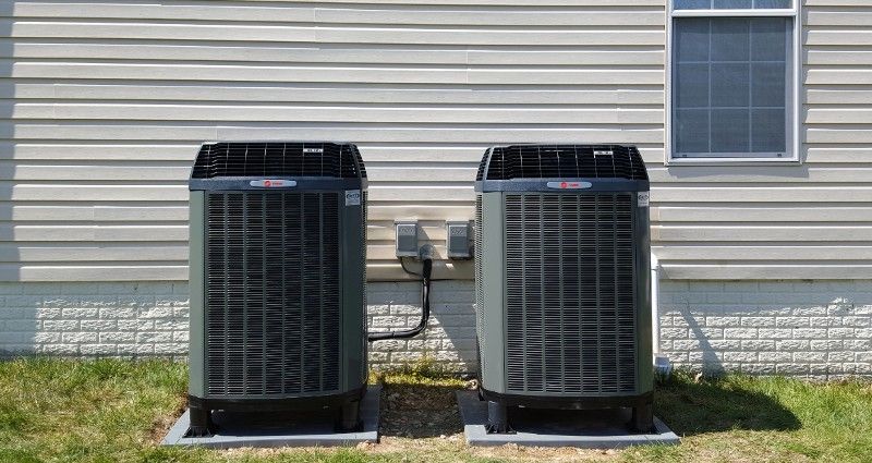 Two air conditioners are sitting on the side of a house.