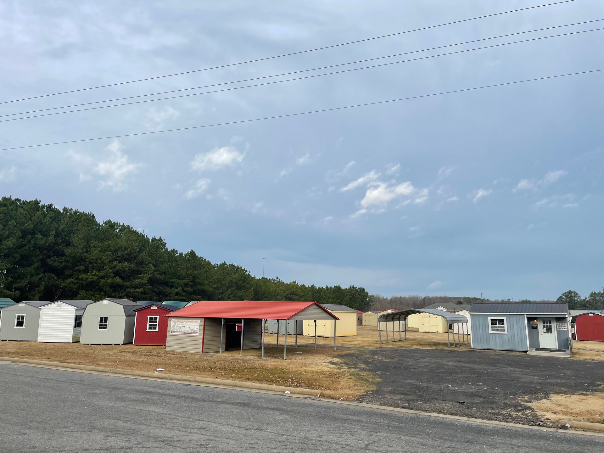 A collection of small storage sheds in various colors, including white, red, and blue, sitting on a gravel lot.