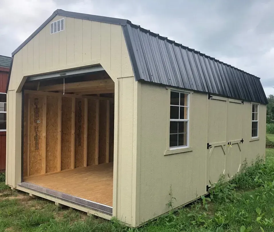 A beige, wooden utility shed with a dark metal roof, a large open front doorway, and two side windows in a grassy field.